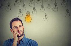 Portrait thinking handsome man looking up with idea light bulb above head isolated on gray wall background
